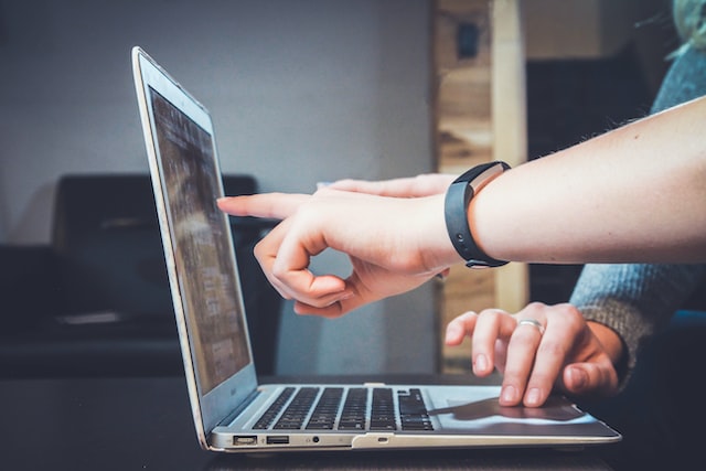 Two white hands pointing at a laptop screen and touching the trackpad